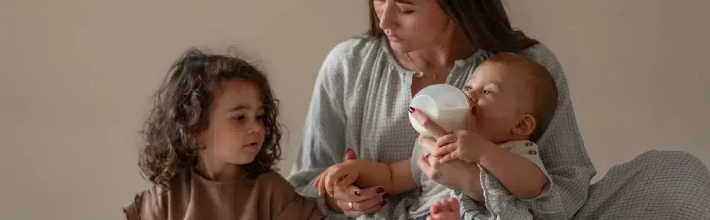 Maman donnant le biberon à son bébé, observée par sa fille ainée